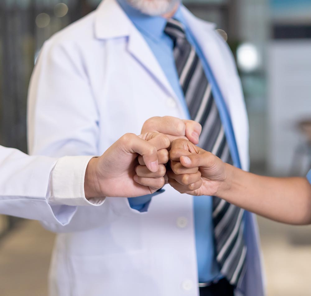 3 people, two of whom are wearing white coats, bump their fists together.