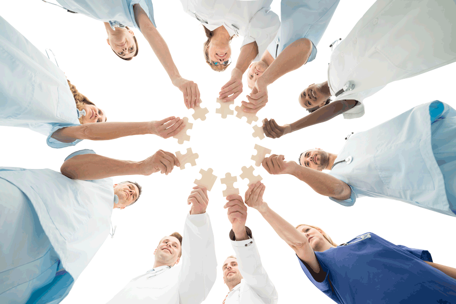 Shot from below, a group of doctors stands in a circle, each one holding a tan puzzle piece out to form an inner circle.